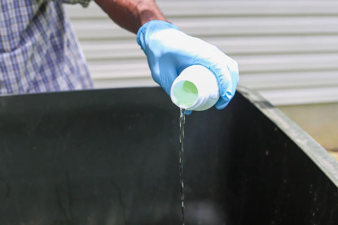 A black African-American man pouring bleach in a dirty garage can