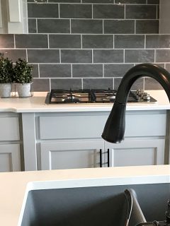 A black pull down faucet inside a modern kitchen with off white countertop matched with gray runway brick backsplash, Touch Faucet Not Working - What To Do?