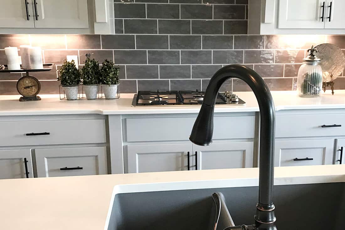 A black pull down faucet inside a modern kitchen with off white countertop matched with gray runway brick backsplash