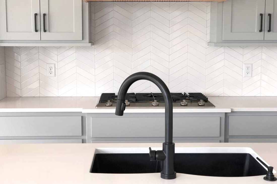 A black pull down faucet inside a modern kitchen with white countertop and light gray cabinets