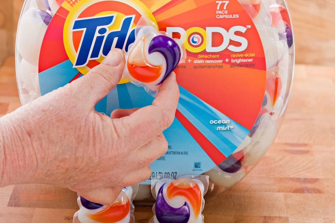 A hand is displaying a Tide Pods which contains pre- measured amounts of detergent,stain remover and brightener for one load of laund