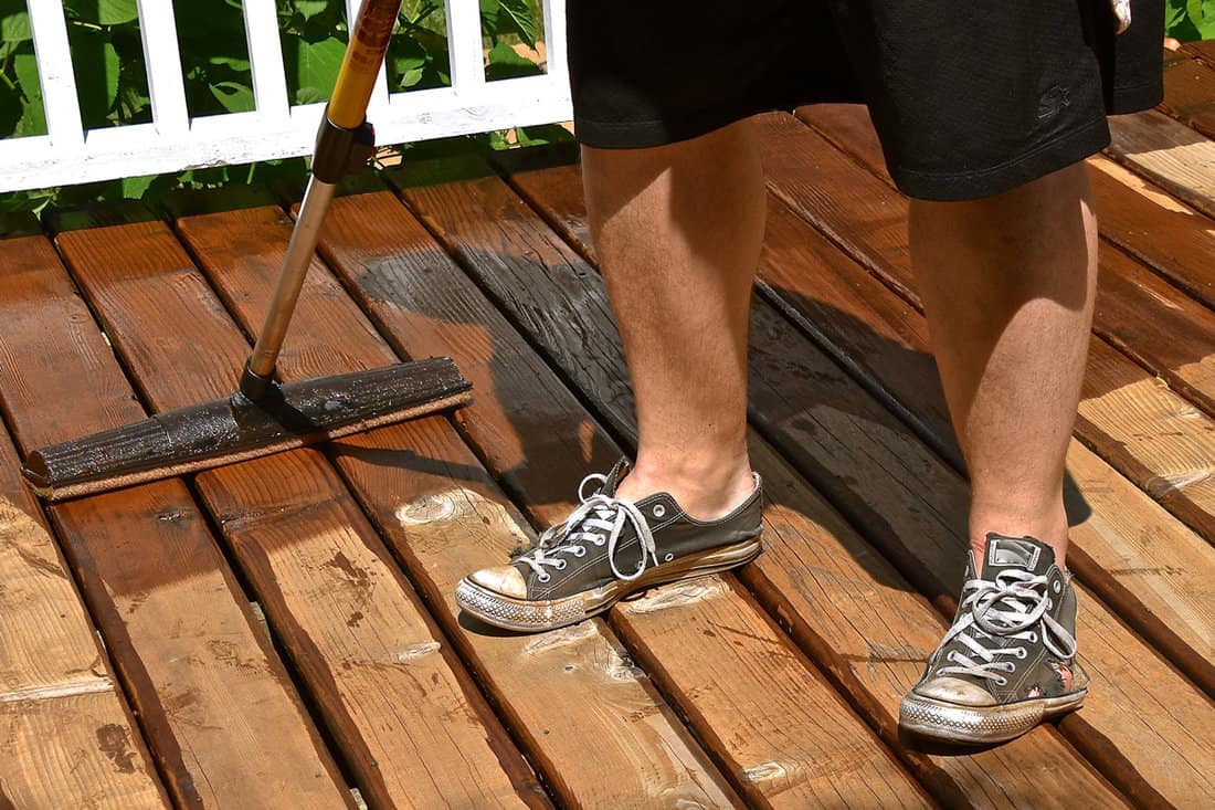 A large sponge on the end of a broom handle is used to apply varnish to an outside deck.