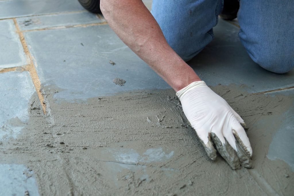 A man spreads wet cement on a cracked sidewalk