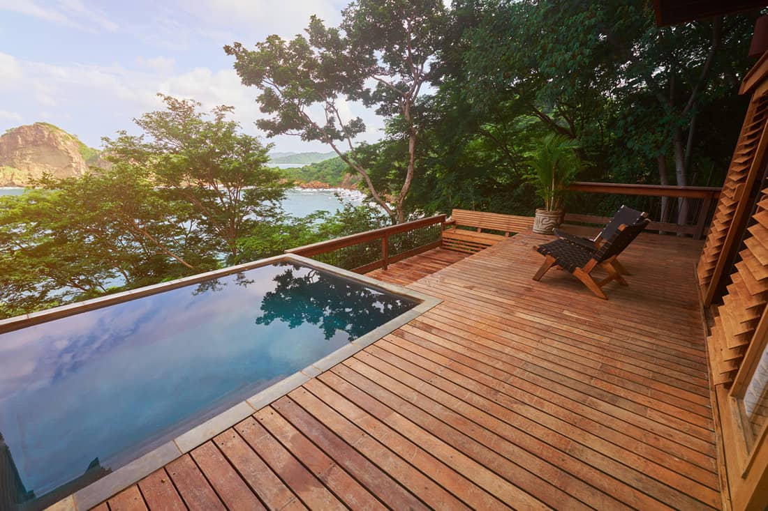 A small wooden deck with a pool on the side providing a gorgeous scenic view of a mountain range