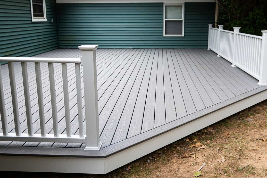 A white wooden deck behind a green house