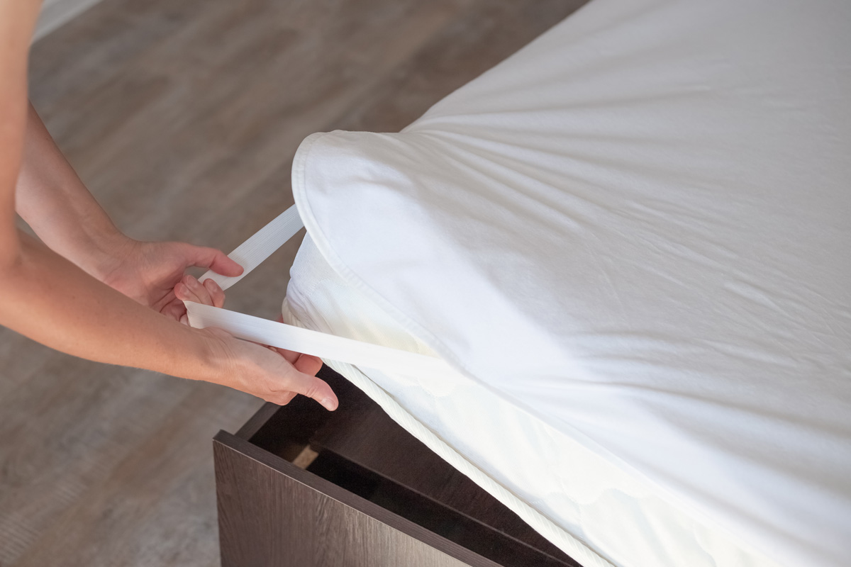 Bed with a high mattress. The woman puts on a protective water-repellent mattress cover.