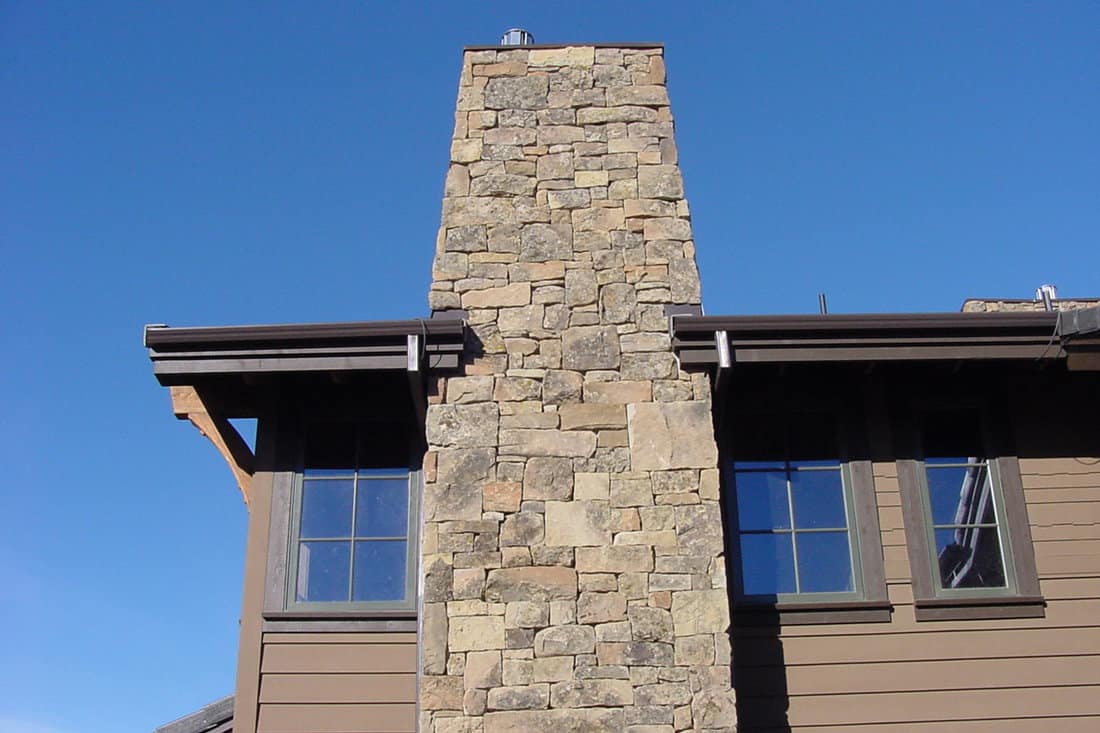 Brown wooden siding and a tall stone veneer decorated on the chimney