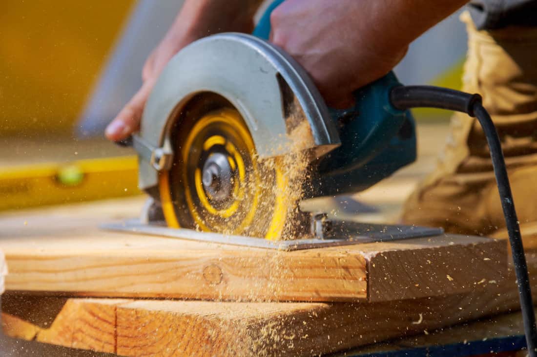 Carpenter using circular saw for cutting wooden boards with hand power tools