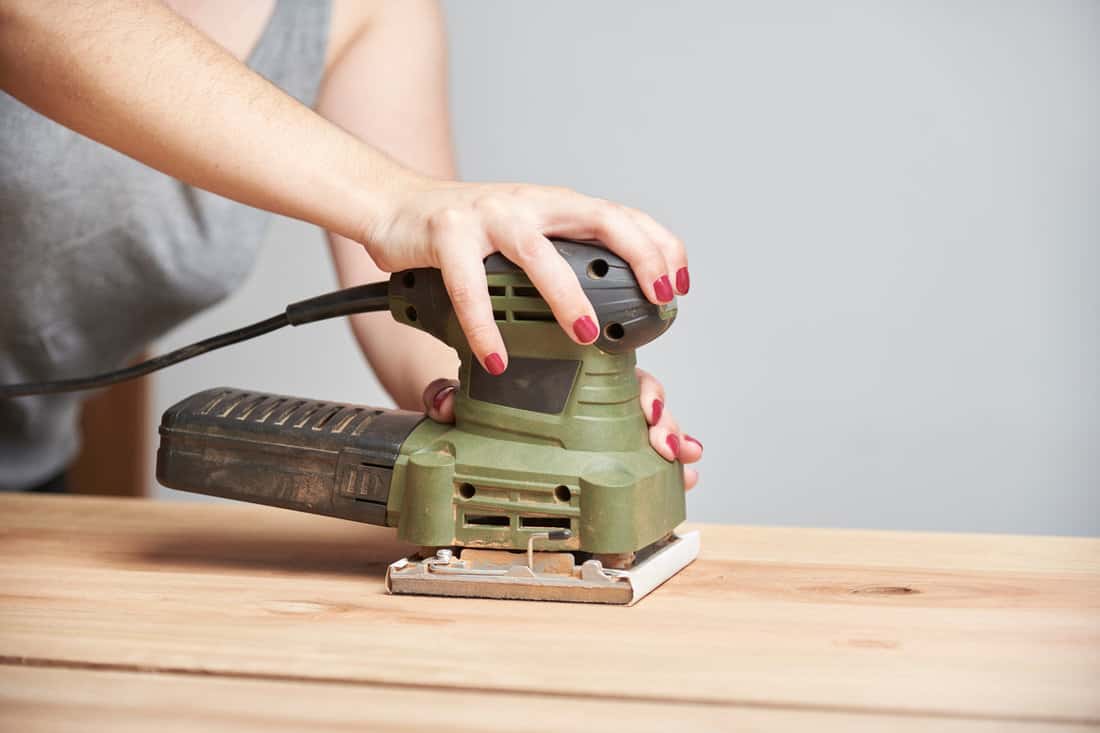 Carpentry work, detail of a young caucasian woman with her nails done sanding wood, using an electric sander.