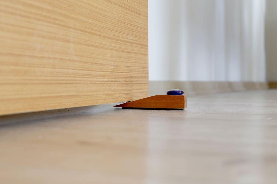Close-up elements of the interior of the apartment. Wooden chrome door stopper on laminate floor — Photo