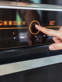 Close up of woman's hand setting temperature control on oven, How To Unlock Whirlpool Oven Door