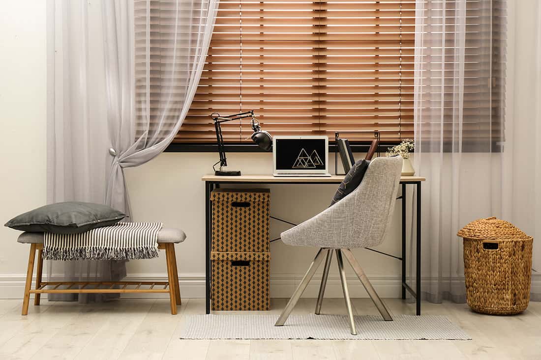 Comfortable workplace near window with horizontal wooden blinds