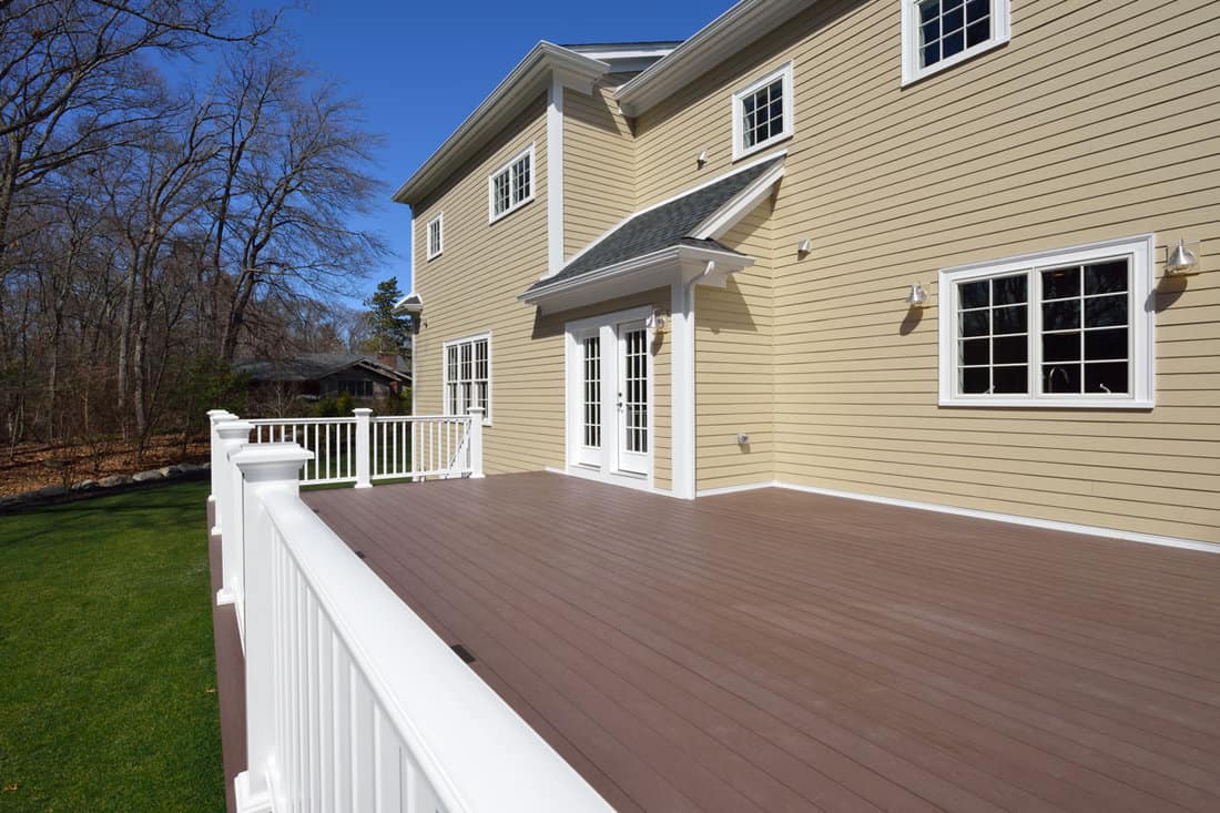 Composite deck in house backyard. Brown boards, white railing posts and veranda