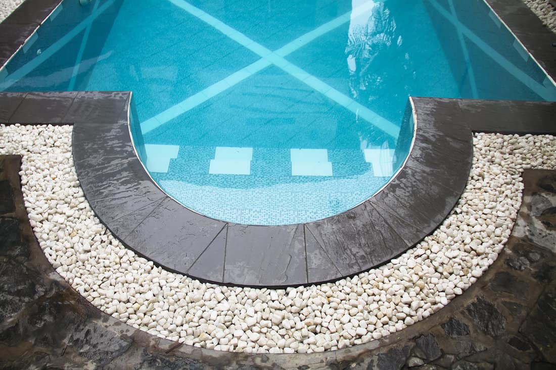 Curve swimming pool gutter with white gravels on top and black slate border