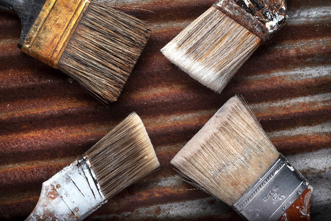 Four old messy paintbrushes lying at an angle on rusty corrugated metal