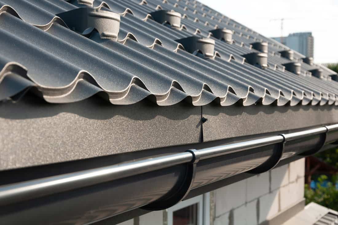 Gray metal roof tiles and rain gutter. House roofing system close-up