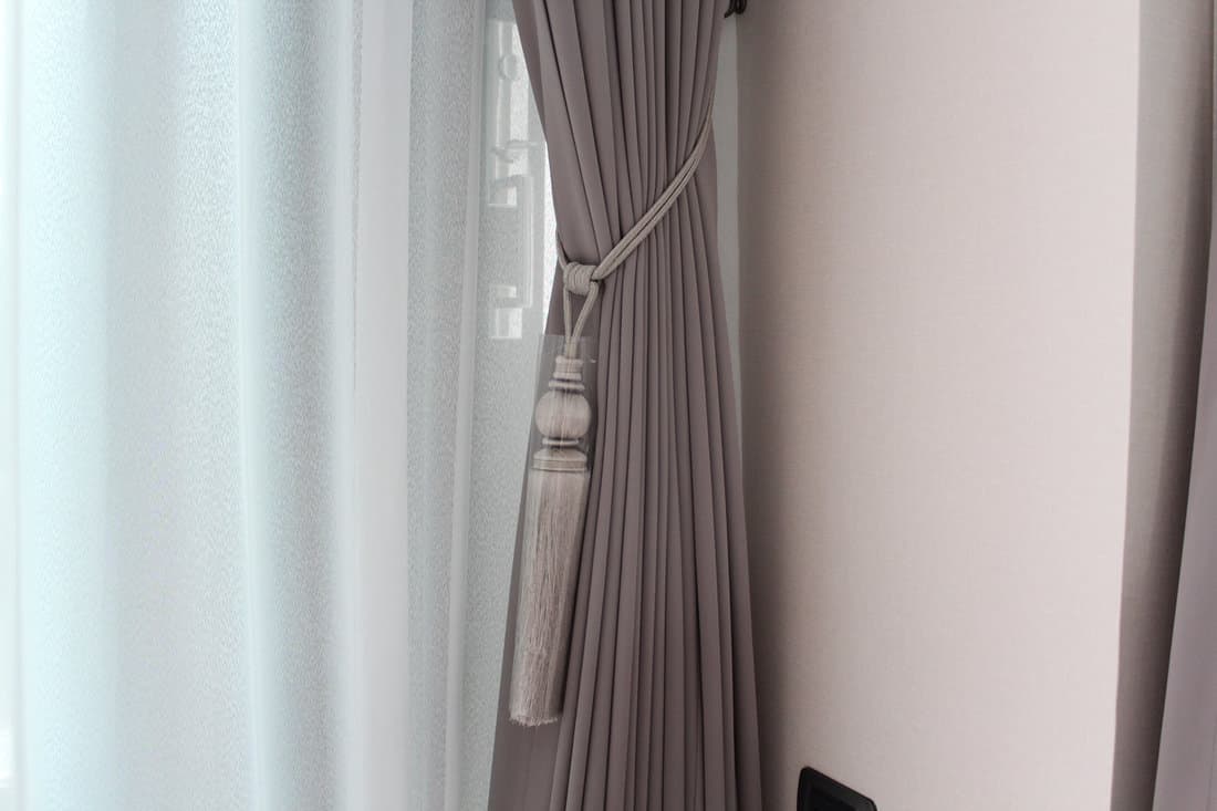 Grey curtains with white sheer curtains with luxury tie back in living room. Mood and tone are in grey and brown colour.