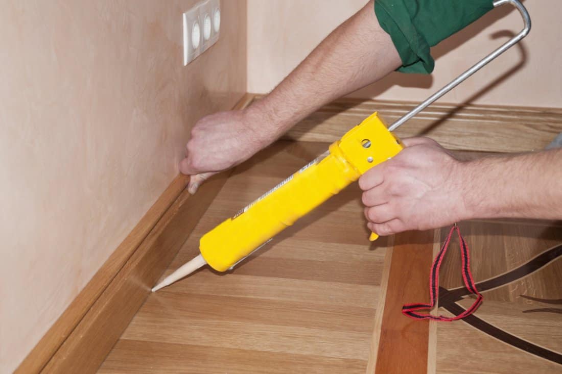 How Do You Fix Messy Caulking Lines - Carpenter on work putting wood parquet skirting board with glue. Caulking Gun in Hand.