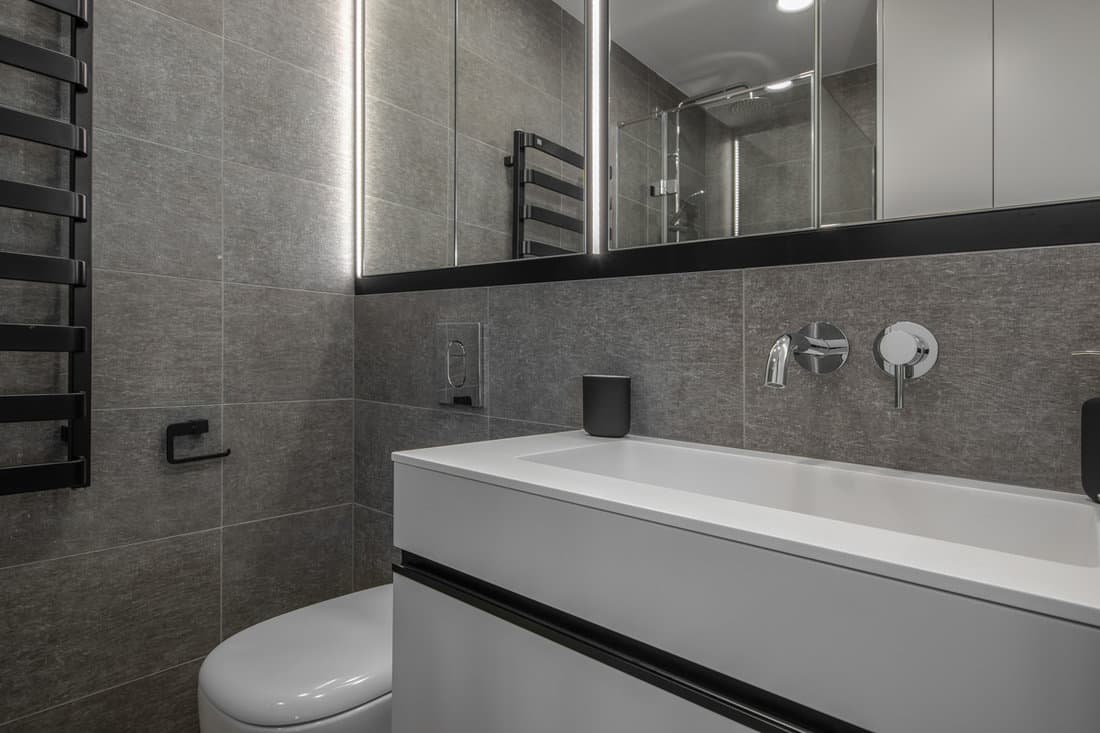 Interior of an ultra gray themed bathroom with white tiled vanity and a huge long span mirror