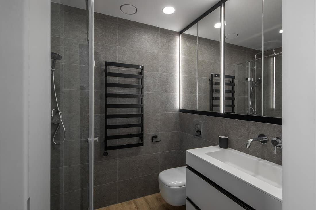 Interior of an ultra modern gray themed bathroom with white vanity and a glass shower head