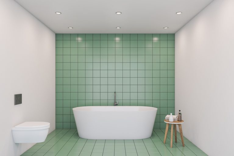 Interior of comfortable bathroom with green tile and white walls, big white bathtub and white toilet - What Color Goes With Green Bathroom Tile