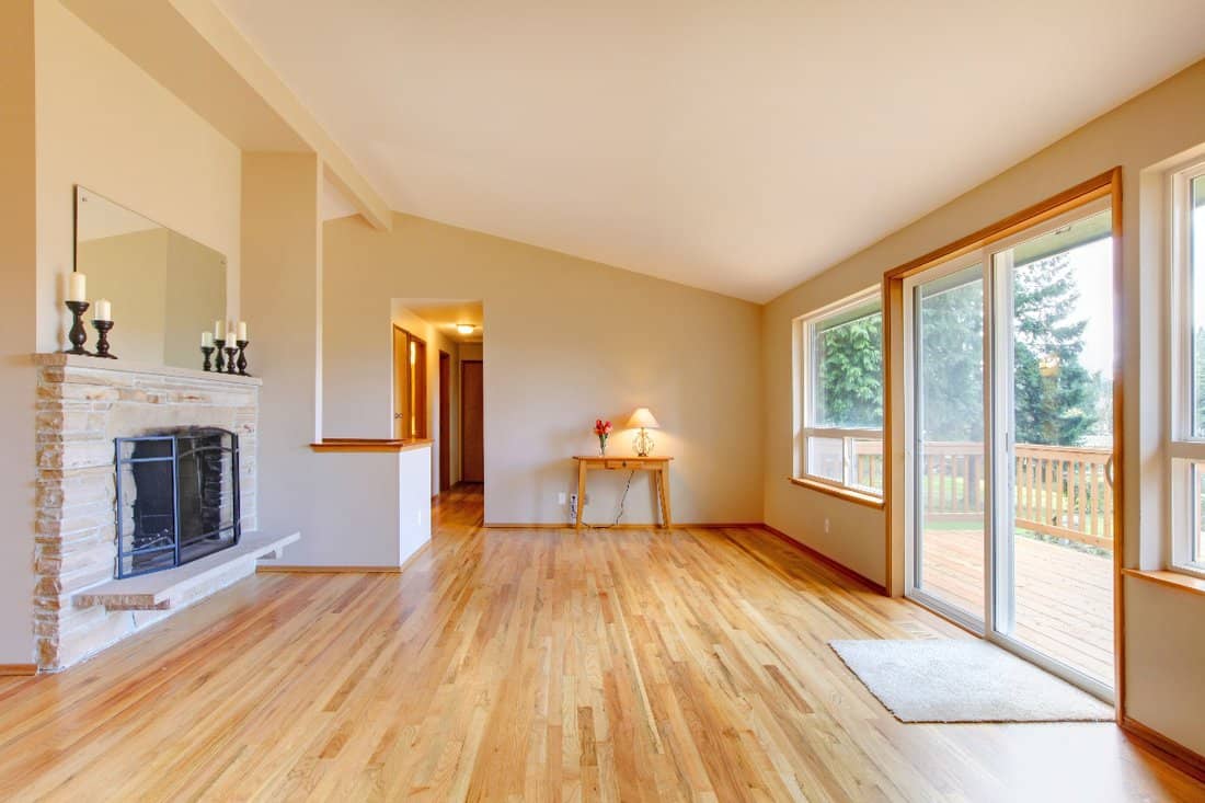 Light Natural Wood - Empty living room with a fireplace, hardwood floor and sliding glass door exit to the deck