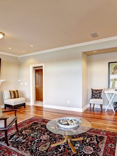 Lovely beige family room with cozy sitting area in wall niche, white column fireplace and accent bright colorful persian rug over polished hardwood floor. Northwest, USA, What Curtains Go With Persian Rugs?