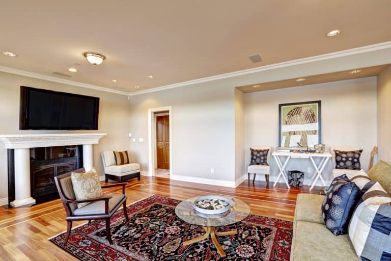 Lovely beige family room with cozy sitting area in wall niche, white column fireplace and accent bright colorful persian rug over polished hardwood floor. Northwest, USA, What Curtains Go With Persian Rugs?