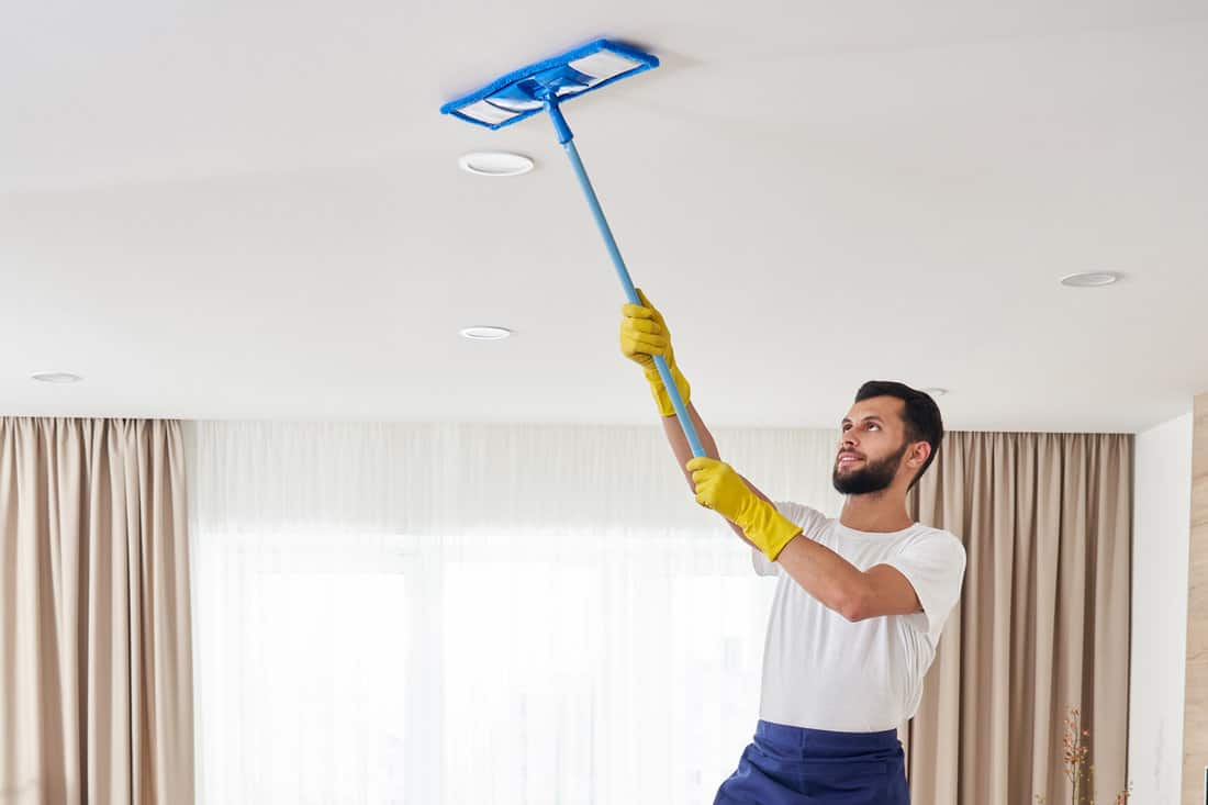 Man holding mop pile, cleaning ceiling in living room.