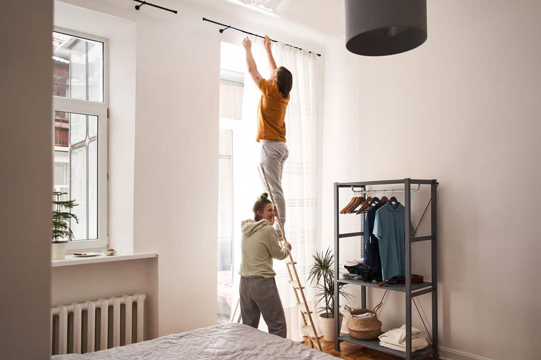 Man standing at the ladder while hanging curtains