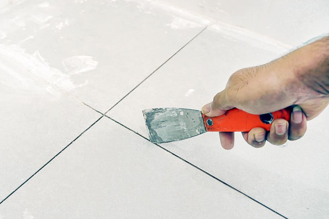 Man uses Trowel to remove old grout. Replace the old grout between the tiles