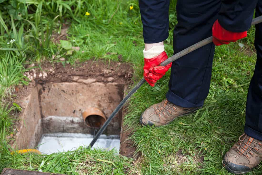 Man with ground open unblocking a drain with a tool stock