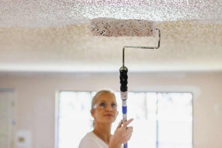 Mature Adult Female Painting Ceiling White With Paint Roller - How To Blend Ceiling Paint To Match Existing Shade