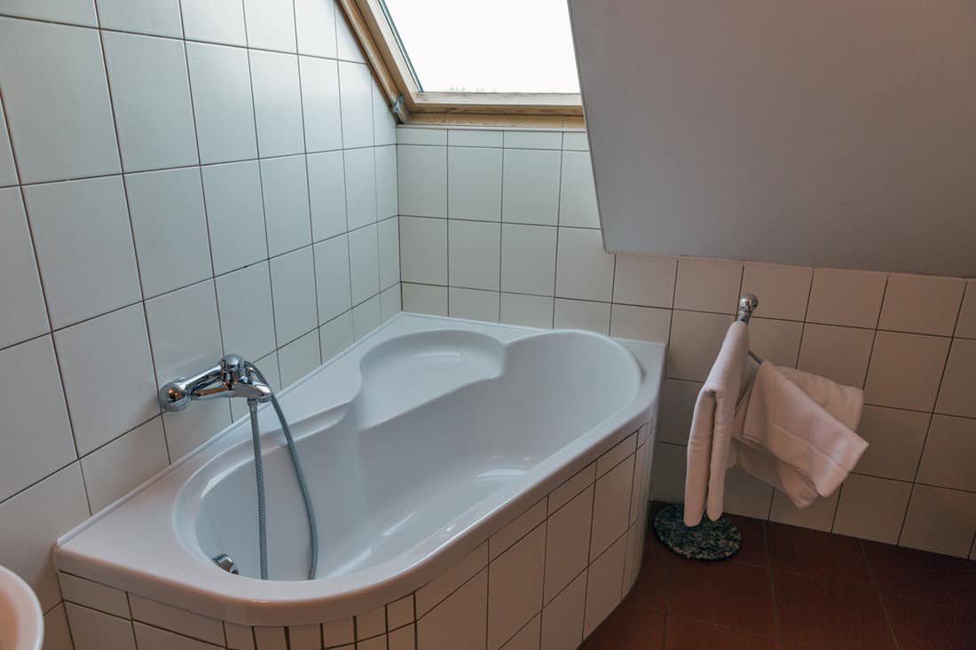Modern white little bathroom with corner bath, towels and window.