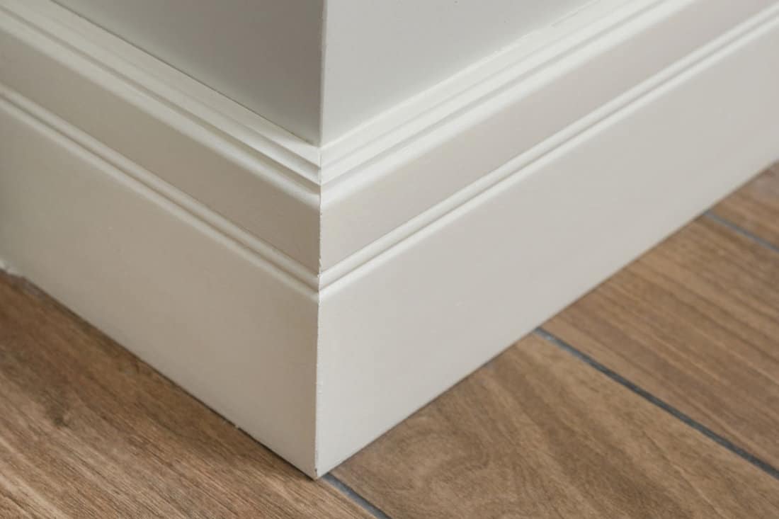 Molding interior of a corner of a baseboard with light matte wall with tiles immitating hardwood flooring
