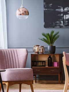 Open space living room interior with poster on grey wall with wainscoting, window with drapes and pink armchair, What Color Curtains Go With Blue Grey Walls?
