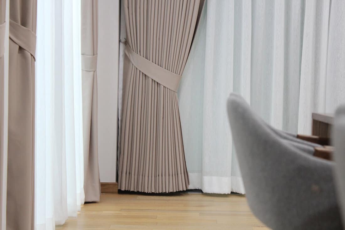 Picture of beautiful neatly tie-back beige fabric curtain drapes over lighten white sheers in the cozy contemporary room. Resident, Elegant, Charming, Interior design, Protecting sun light, Expensive.