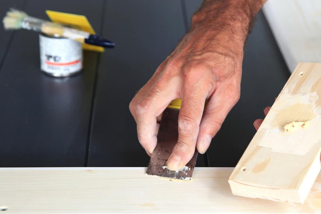 Preparation woodwork. Close-up details Putty knife in man's hand. DIY worker applying filler to the wood. Removing holes from a wood surface. Application of putty.