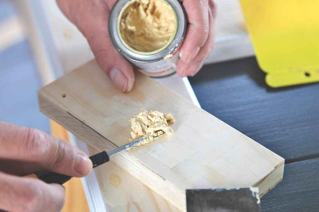 Preparation woodwork. Close-up putty cans in man's hand. DIY worker applying filler to the wood. Removing holes from a wood surface. Application of putty.