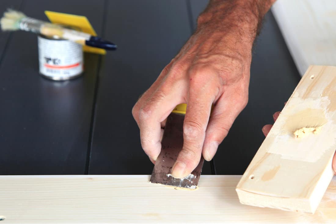 Preparation woodwork. Close-up details Putty knife in man's hand. DIY worker applying filler to the wood. Removing holes from a wood surface. Application of putty. 