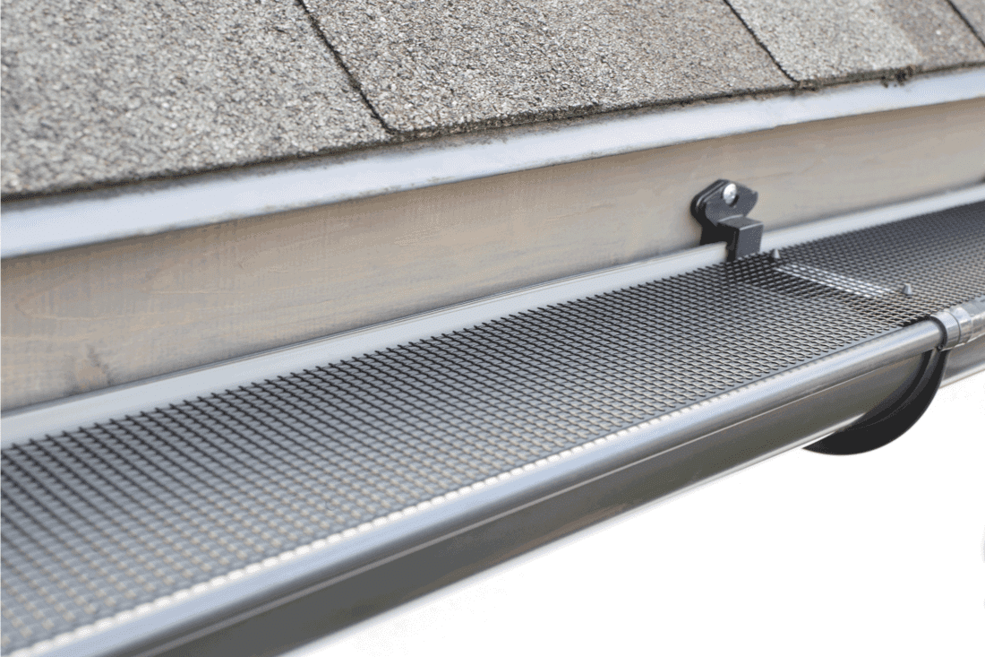 Plastic guard over new dark grey plastic rain gutter on asphalt shingles roof 