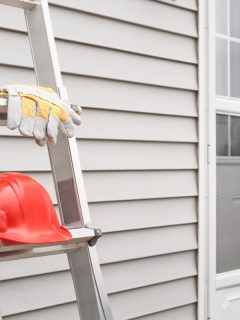 Red hard hat and working gloves on a ladder with a background of house siding - Red hard hat and working gloves on a ladder with a background of house siding.