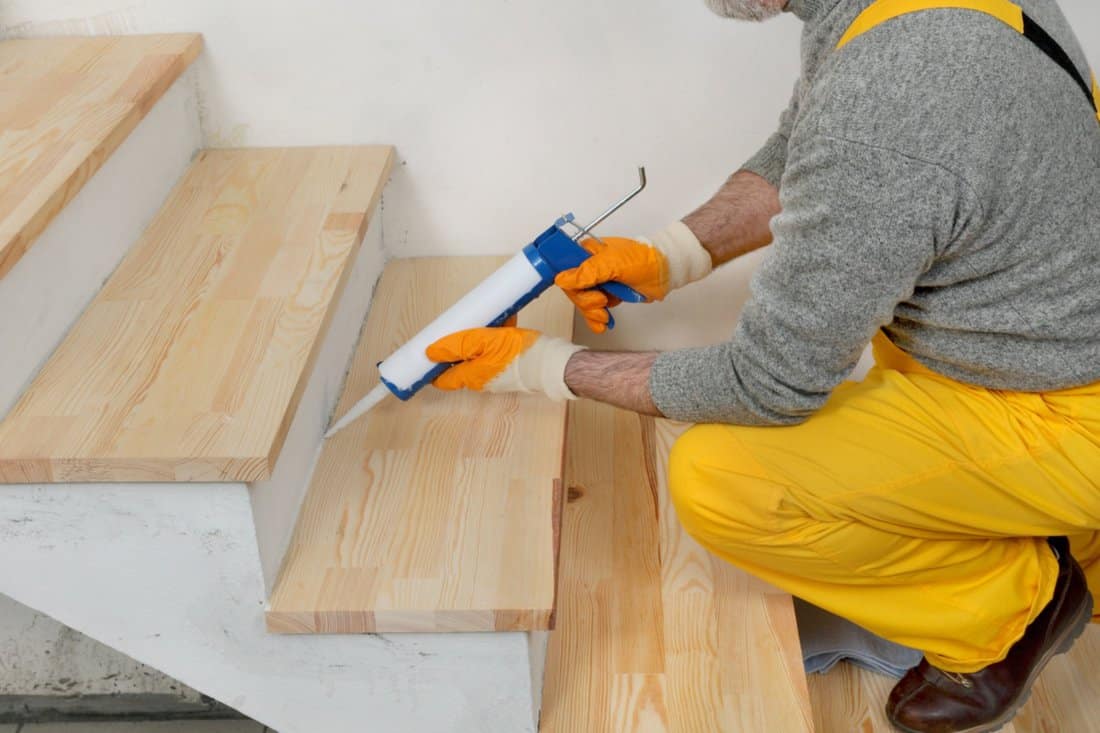 Steps To Apply Caulk - Construction worker caulking wooden stairs with silicone glue using cartridge
