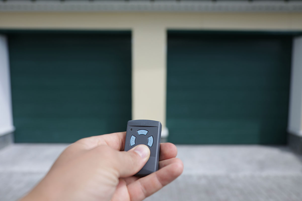 The man holds in his hand a remote control that opens the door of a double garage