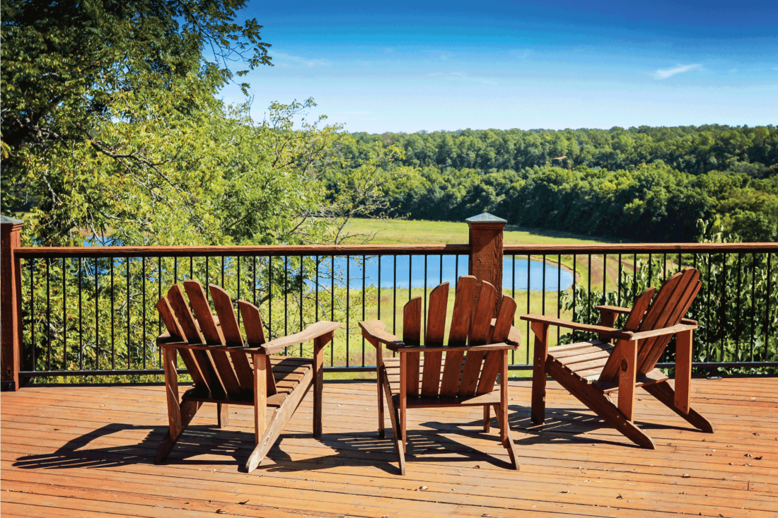 Three adirondack chairs on a deck overlooking a lake