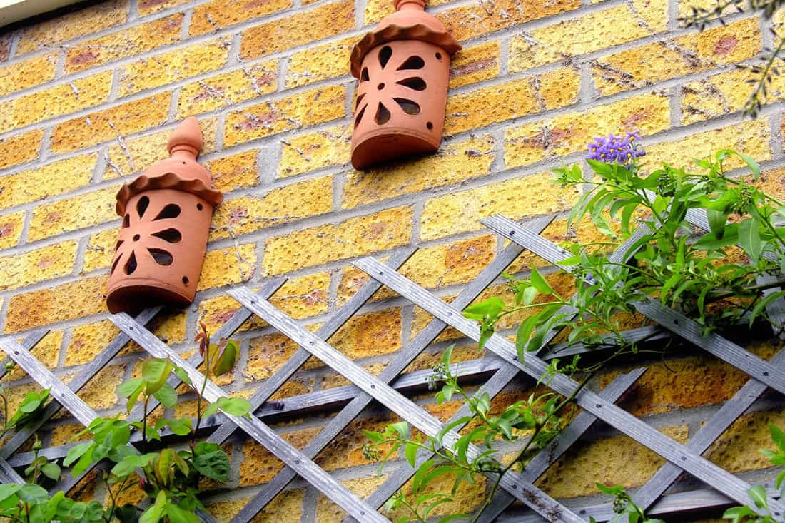 Two clay lanterns on brick wall above trellis work