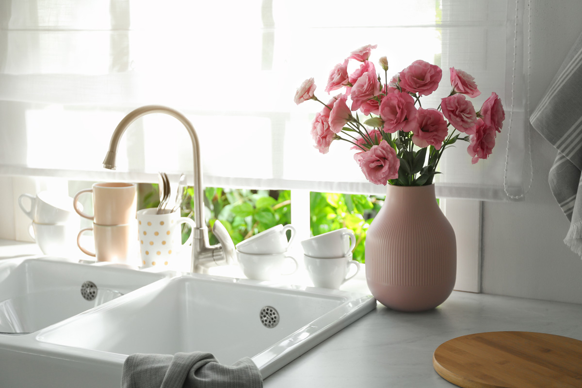 Vase with flowers on countertop near sink against window in kitchen