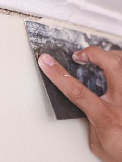 A handyman applies putty or filler to cover the gap between a wood cornice and a concrete wall with a trowel. Home improvement or renovate, How To Use Wood Filler On Corners