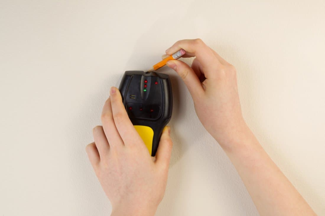 Ways To Find Wall Studs - Photo of female hands holding using stud finder and pencil against interior home white wall