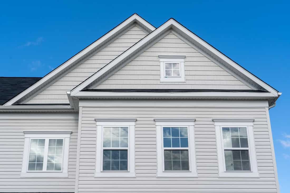 White wood accents along roof lines and above windows with using vinyl boards triangle gable covered by horizontal vinyl siding, fascia and an attic white window frame